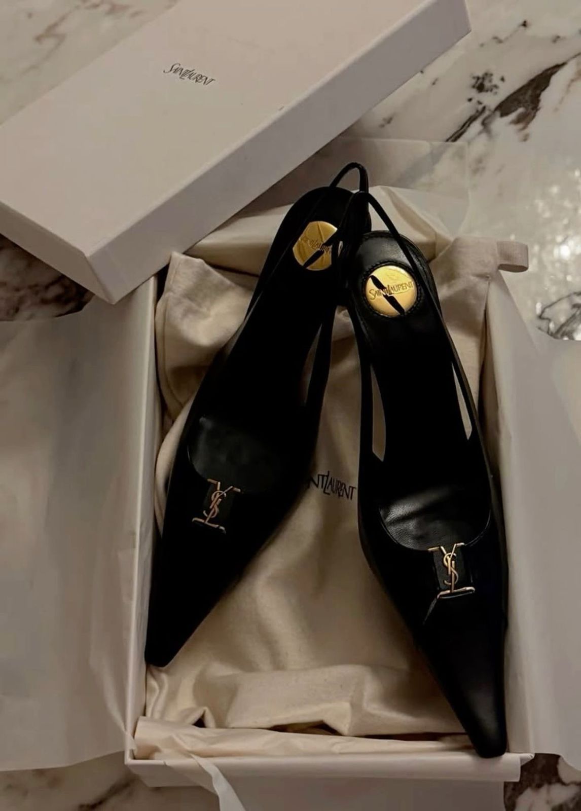 YSL Babylone Women’s PumpsBlack high-heeled shoes with gold accents in a branded box on a marble surface