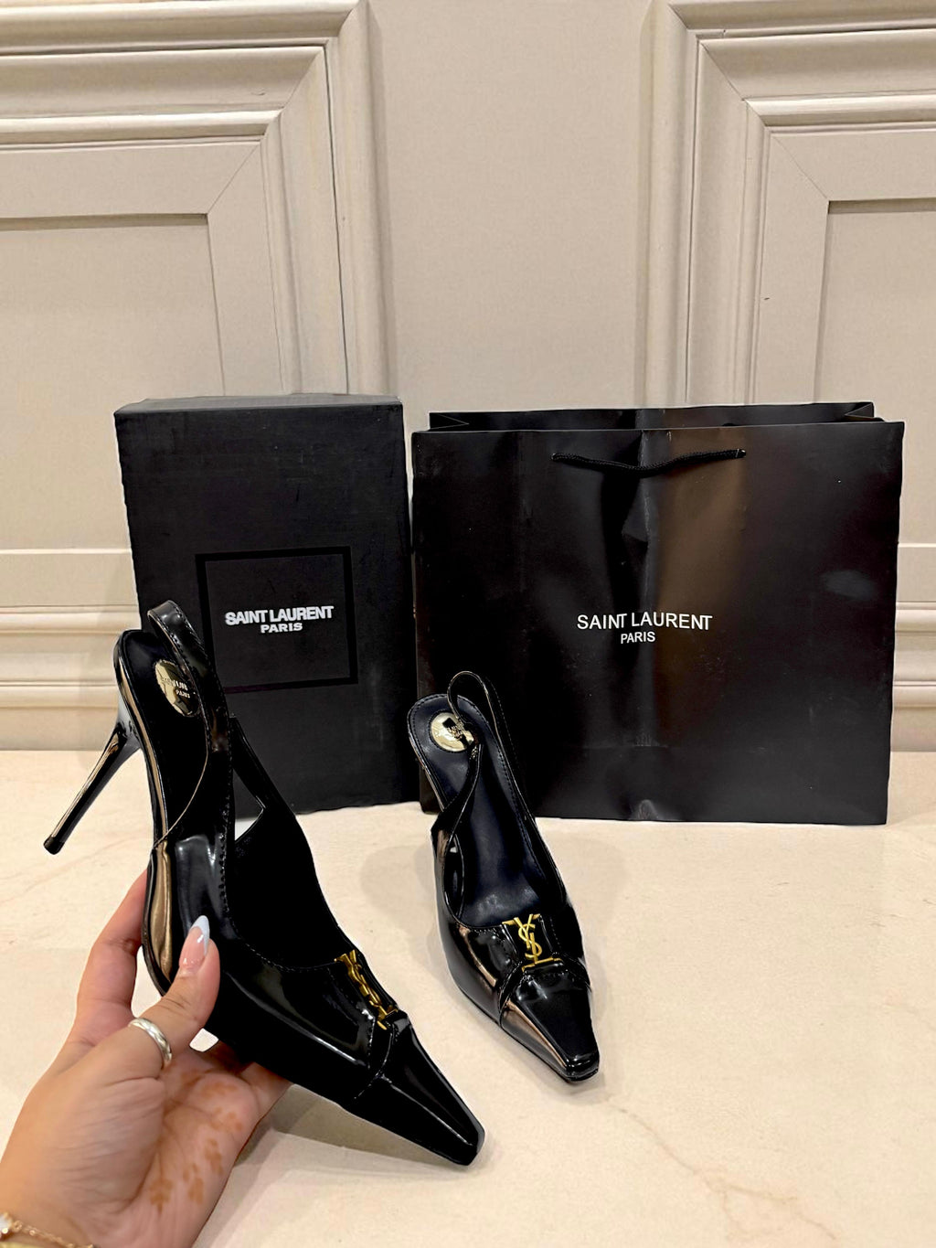 YSL Babylone Women’s Pumps Black high-heeled shoes with Saint Laurent packaging on a light-colored surface.