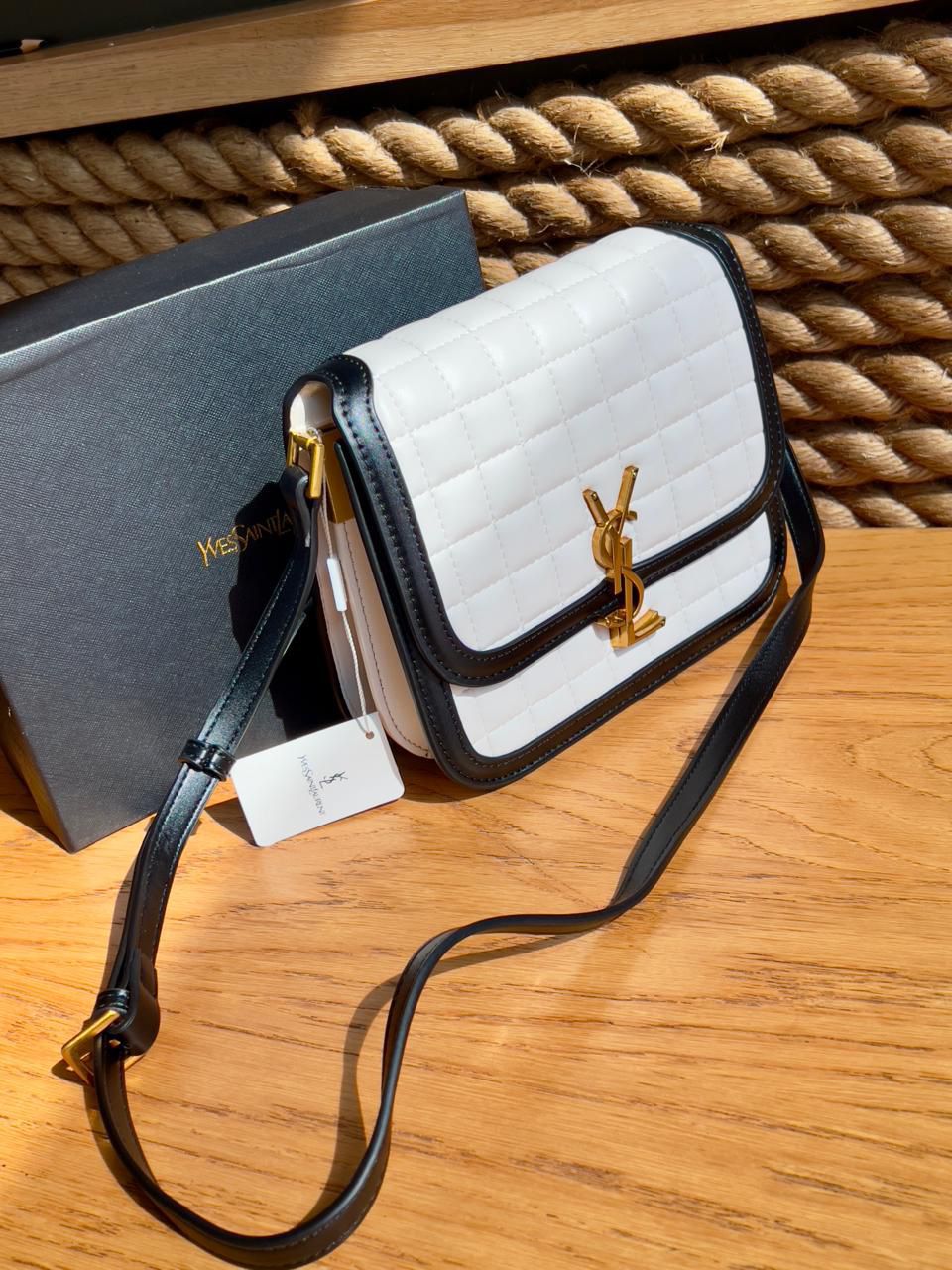 White Yves Saint Laurent YSL Premium Shoulder Bag handbag with black accents and a visible brand logo on a wooden surface.
