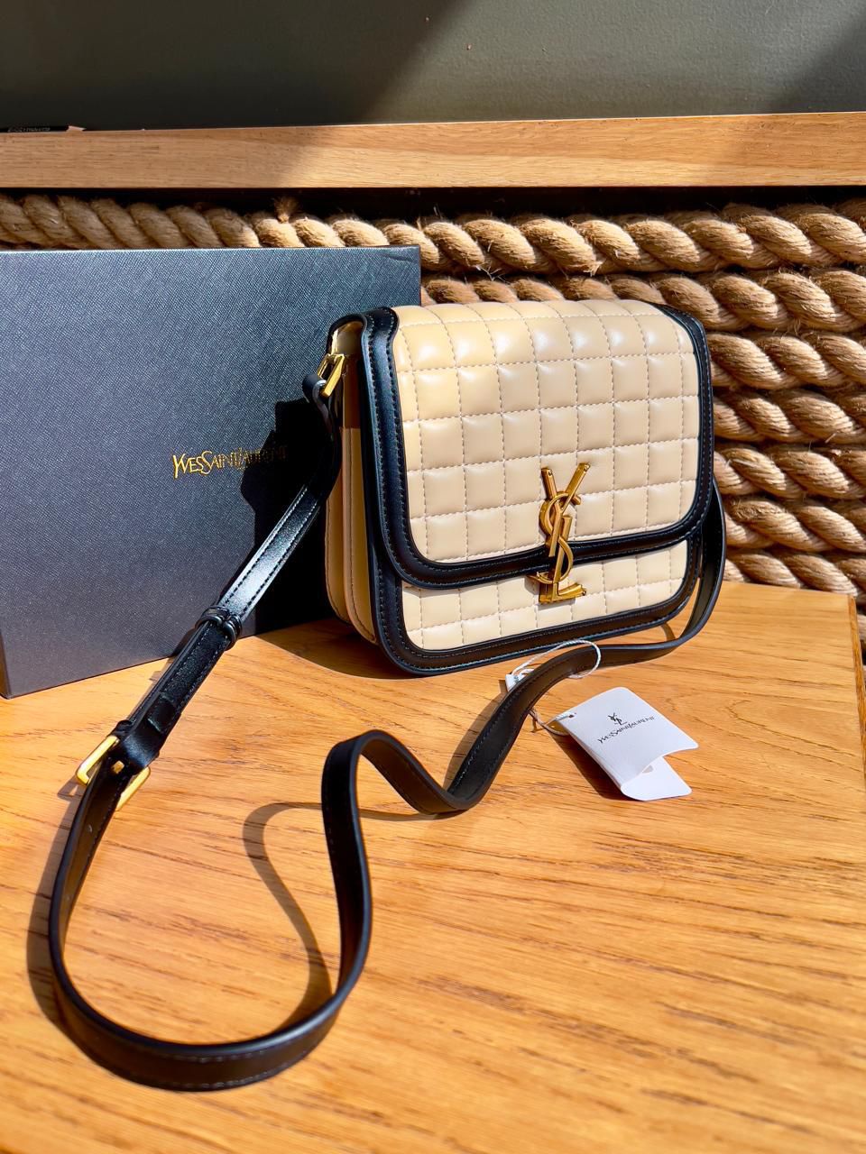 Beige Yves Saint Laurent YSL Premium Shoulder Bag handbag with black strap on a wooden surface, with Yves Saint Laurent logo visible.