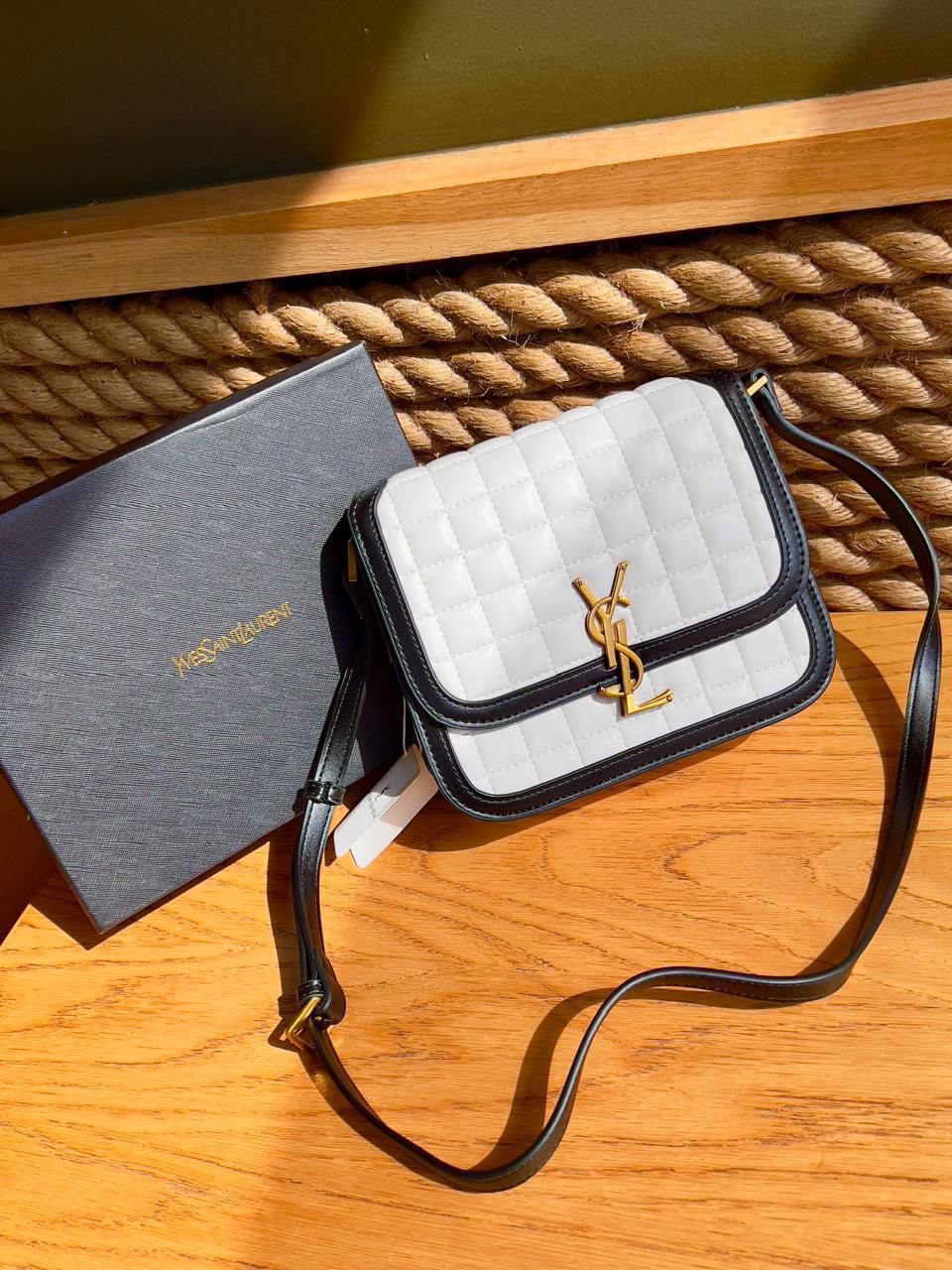 White Yves Saint Laurent YSL Premium Shoulder Bag handbag with black accents and a brand logo on a wooden surface next to a branded box.