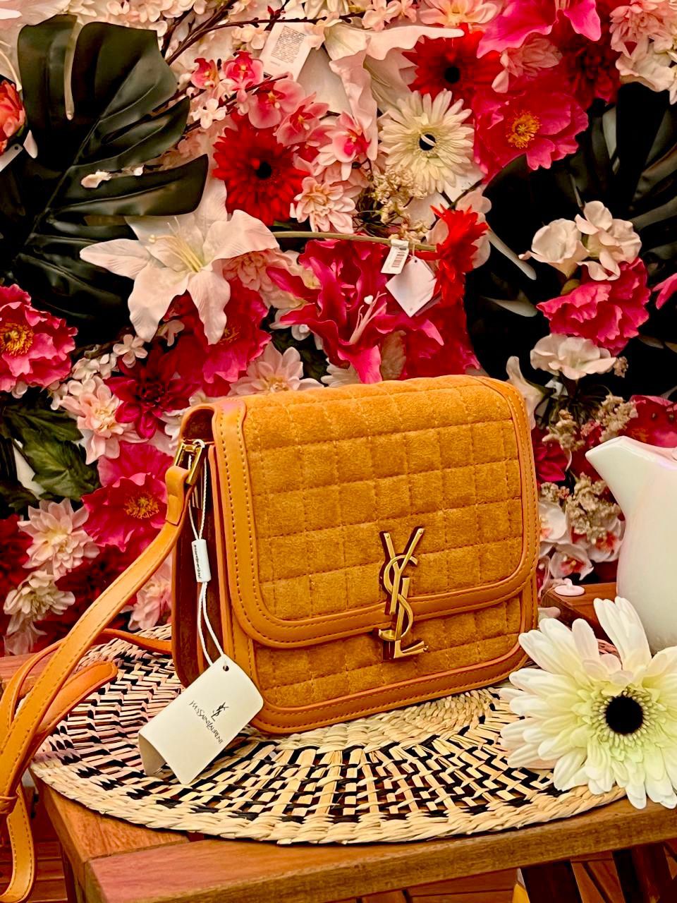 Brown Yves Saint Laurent YSL Premium Shoulder Bag quilted handbag with a brand logo on a decorative table with flowers