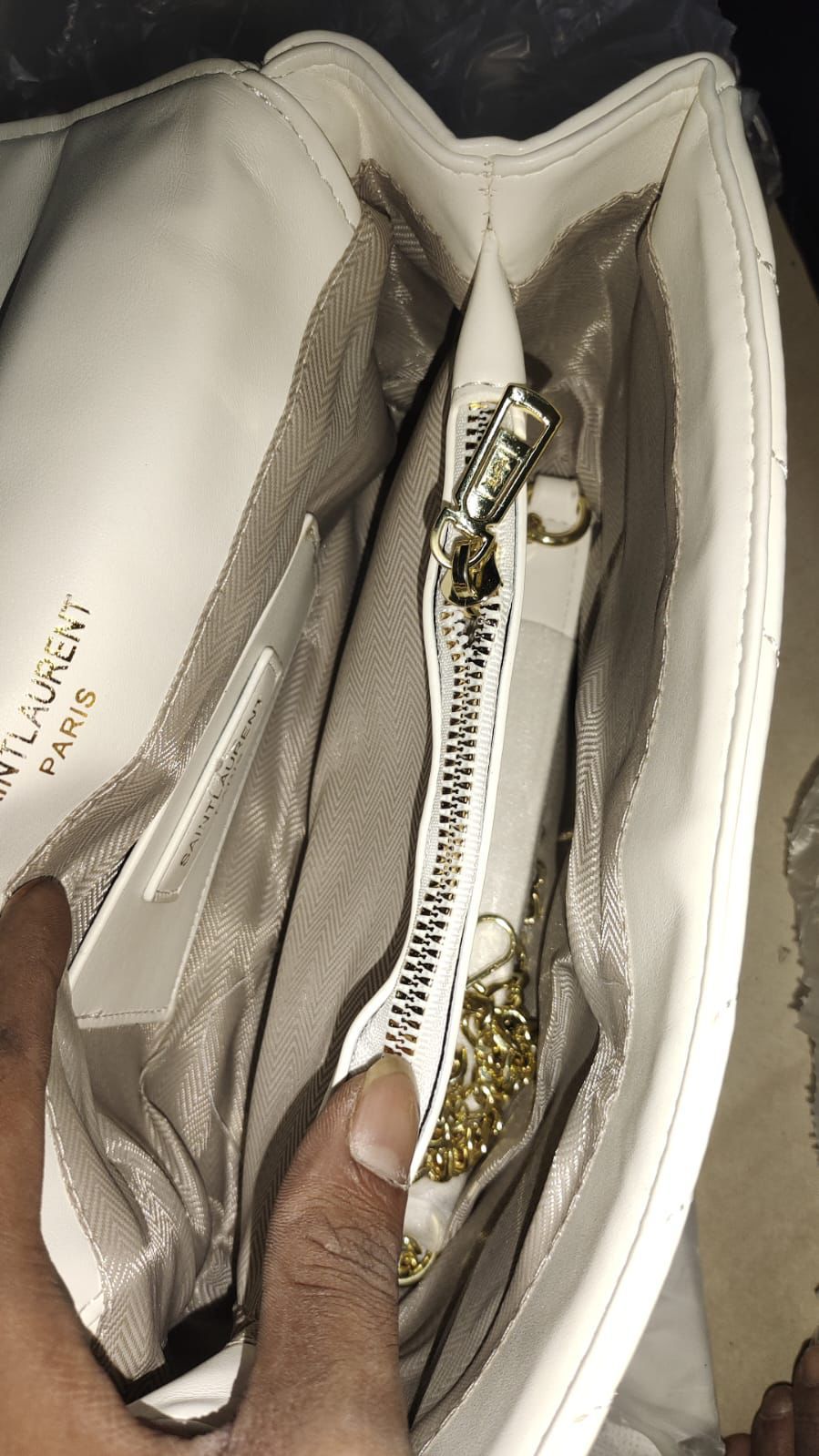 White YSL Saint Laurent Sling Bag Close-up of a YSL handbag with gold zipper being held by a hand.