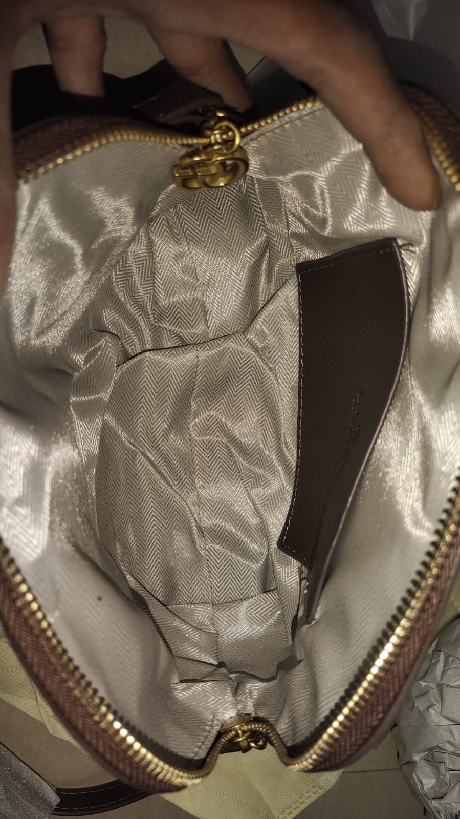 Close-up of a hand holding a gold zipper with a textured surface.