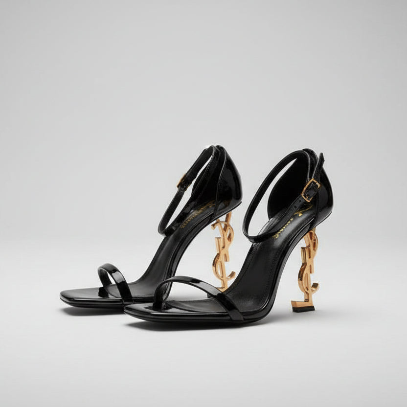 YSL High Heel Sandals for Women Black high-heeled shoes with gold chain details on a textured white surface