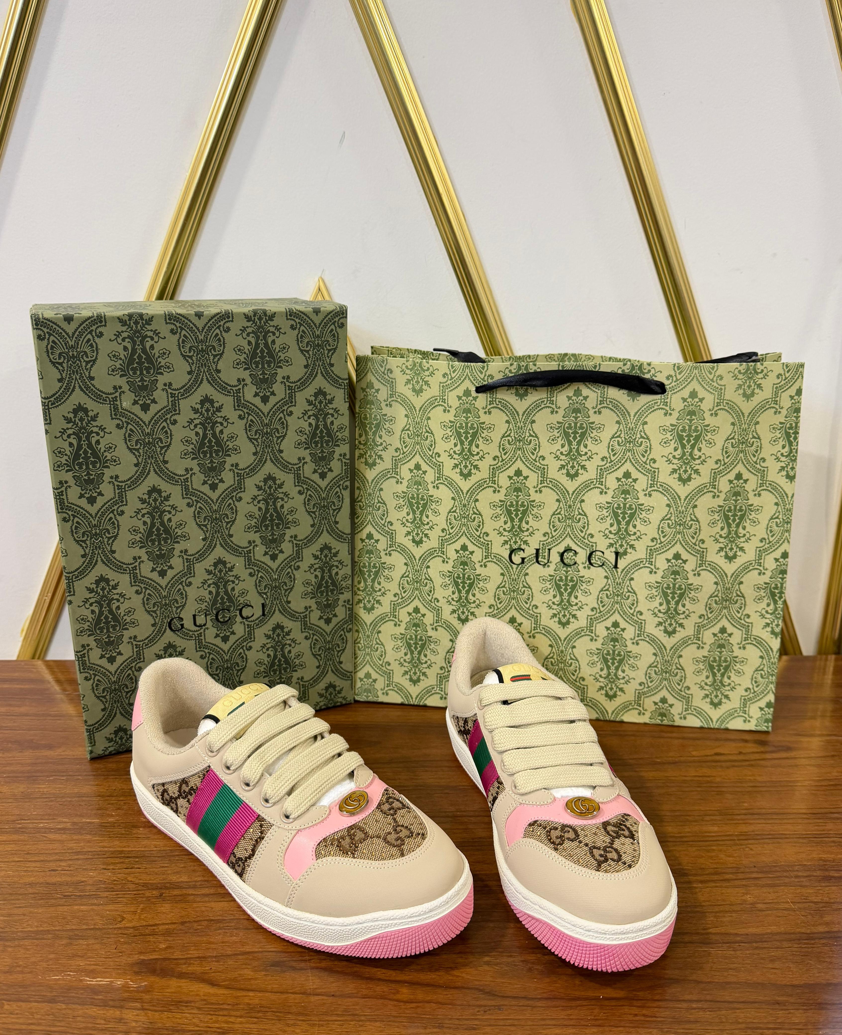 Gucci Women’s Premium Sneakers Beige sneakers with colorful accents next to a Gucci shopping bag and box on a wooden surface.