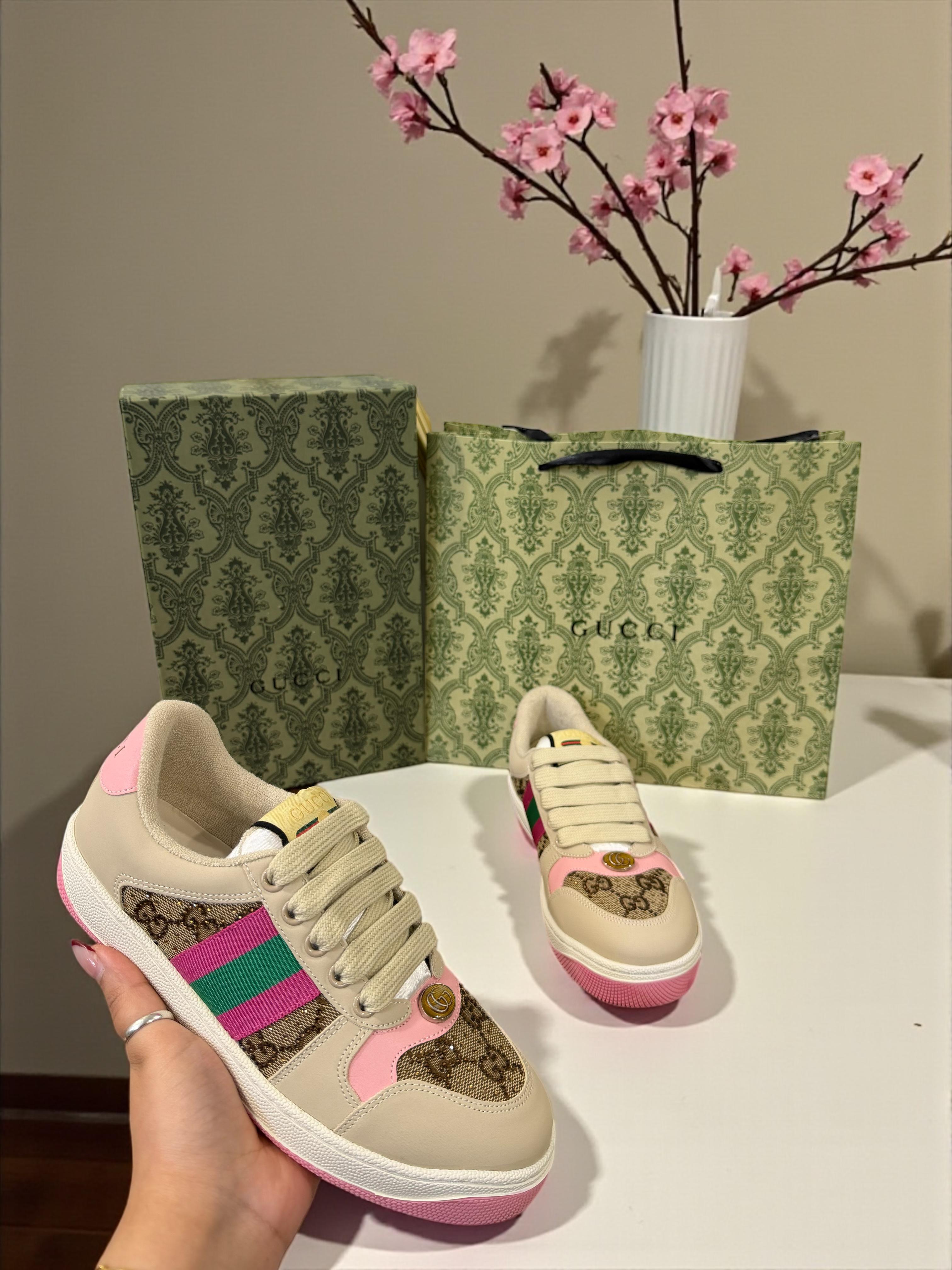 Gucci Women’s Premium Sneakers Beige sneakers with pink and green accents held by a hand, Gucci box, and decorative vase with pink flowers in the background.