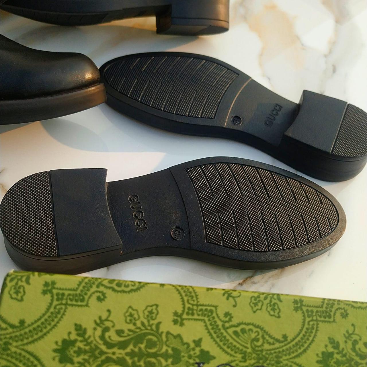 Close-up of black shoe soles on a white surface with a green patterned fabric underneath.