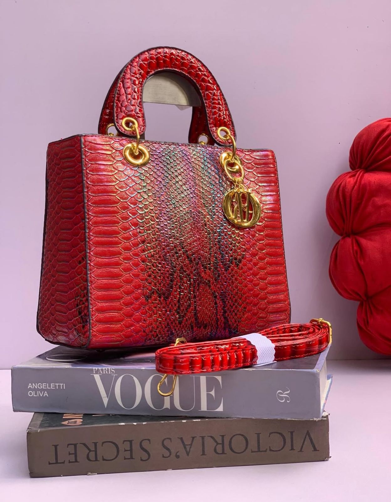 Red Lady Dior Premium Handbag textured handbag with gold accents on top of books, with a red garment in the background.