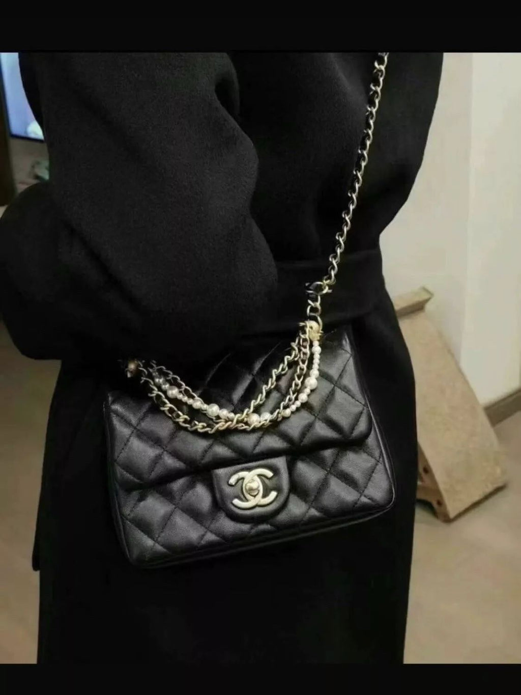 Black Chanel Mini Flap Bag quilted handbag with gold chain strap held by a person wearing a black coat.