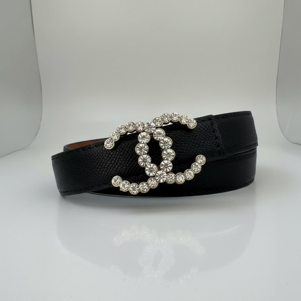Black Chanel Studded Reversible Belt Black sandal with a decorative strap featuring crystals on a marble surface.