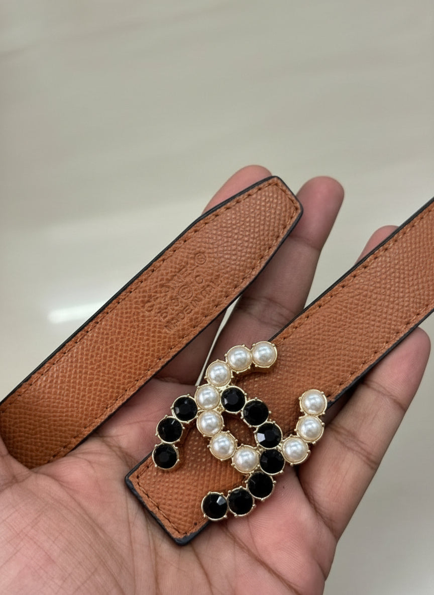 Brown Chanel Studded Reversible Belt Brown leather strap with decorative black and pearl embellishments held by a hand.