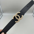 Black Chanel Studded Reversible Belt .Black belt with pearl embellishments held by a hand, with additional belts in the background.