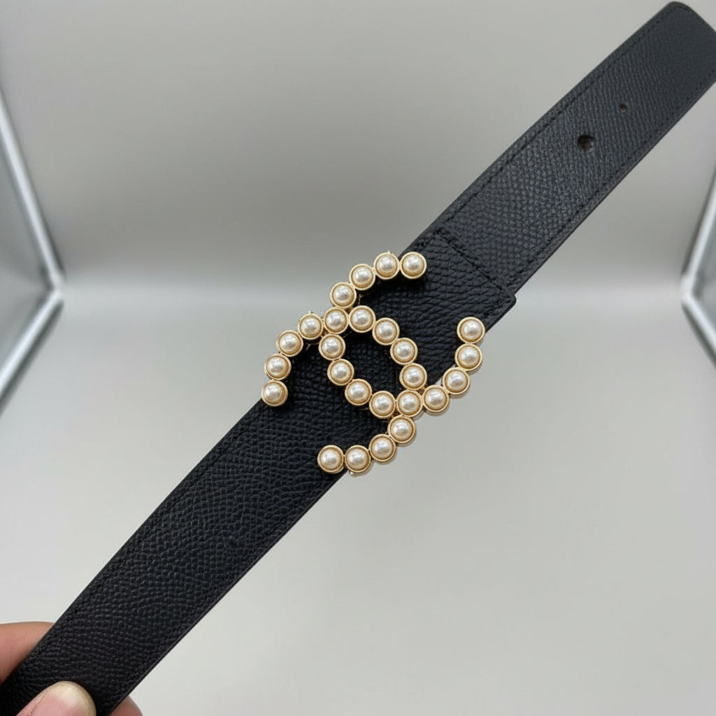 Black Chanel Studded Reversible Belt .Black belt with pearl embellishments held by a hand, with additional belts in the background.