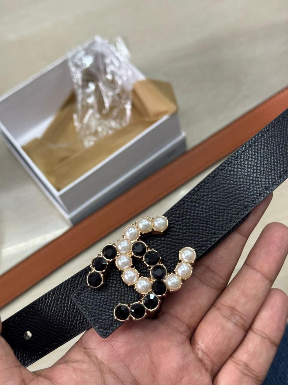 Black Chanel Studded Reversible Belt Black belt with decorative buckle held by a hand, with a white box in the background.