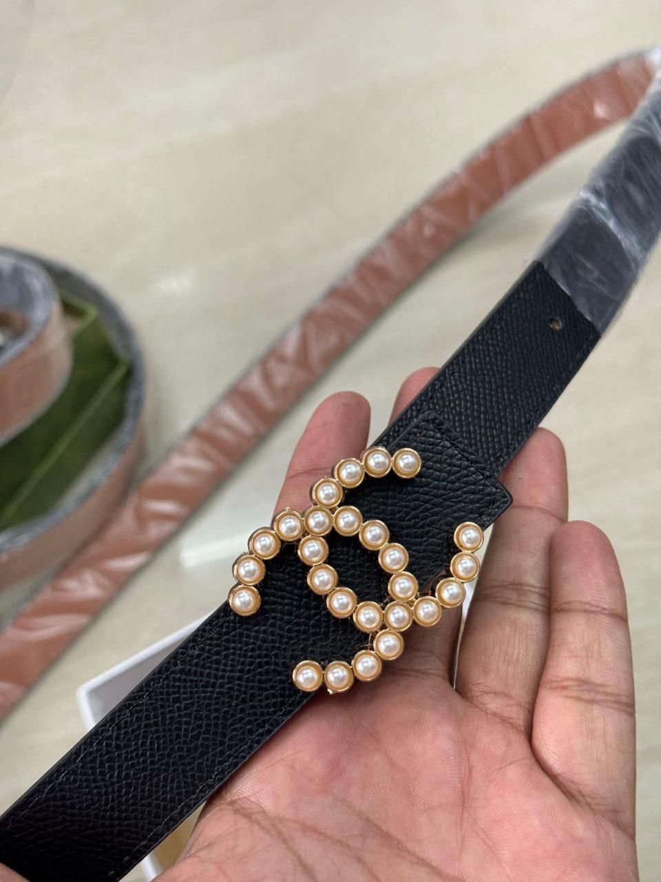 Brown Chanel Studded Reversible Belt Black belt with pearl embellishments held by a hand, with additional belts in the background.