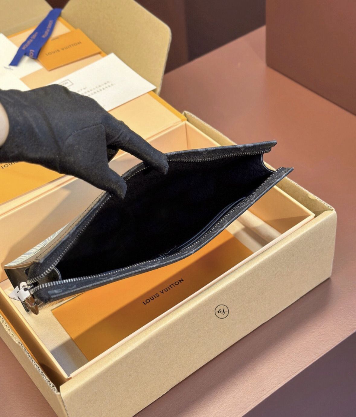 Louis Vuitton Unisex Reverse Pochette Hand opening a Louis Vuitton pouch in a branded box with a gloved hand