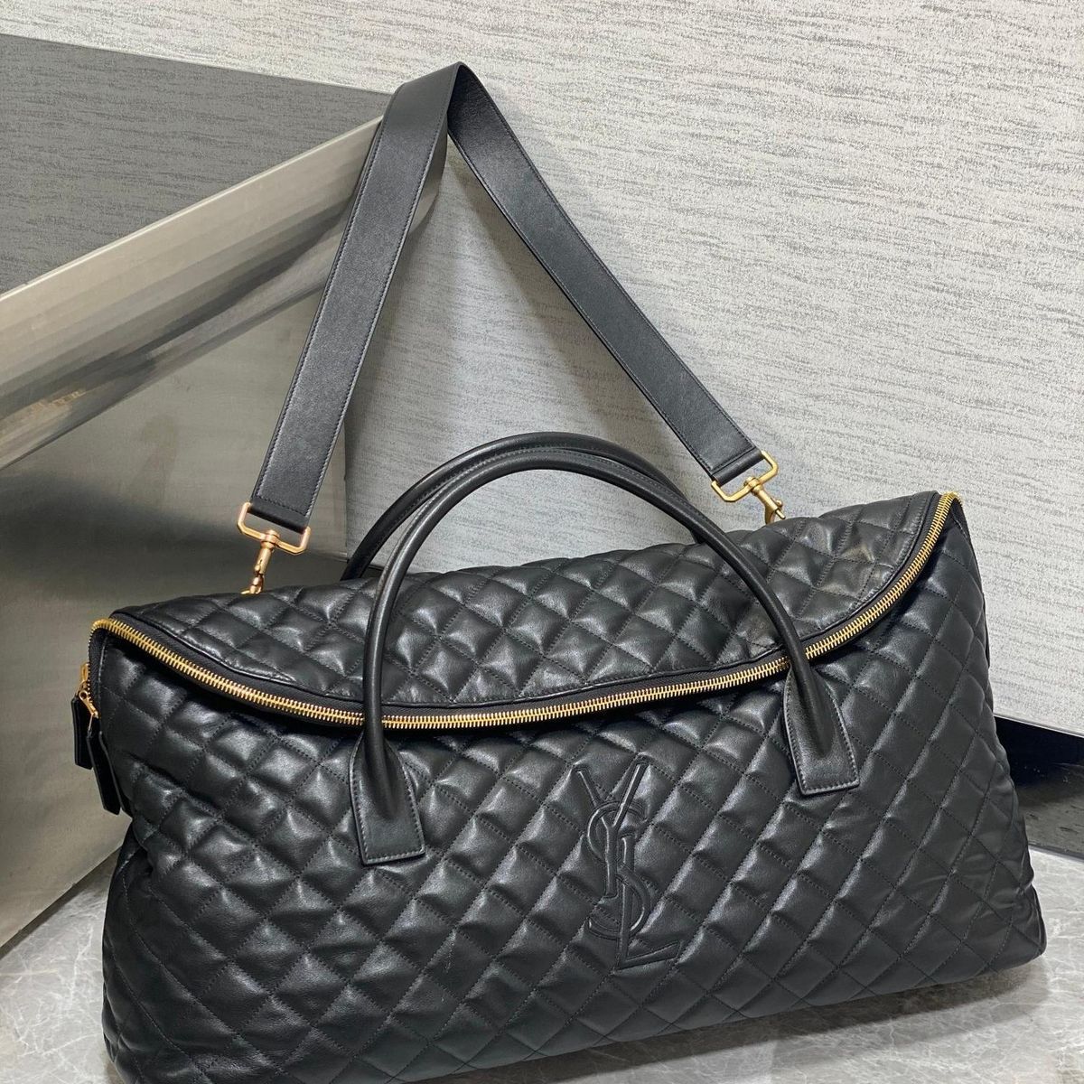 Black YSL Giant Quilted Leather Weekend Duffle Bag Black quilted handbag with gold accents on a light gray background