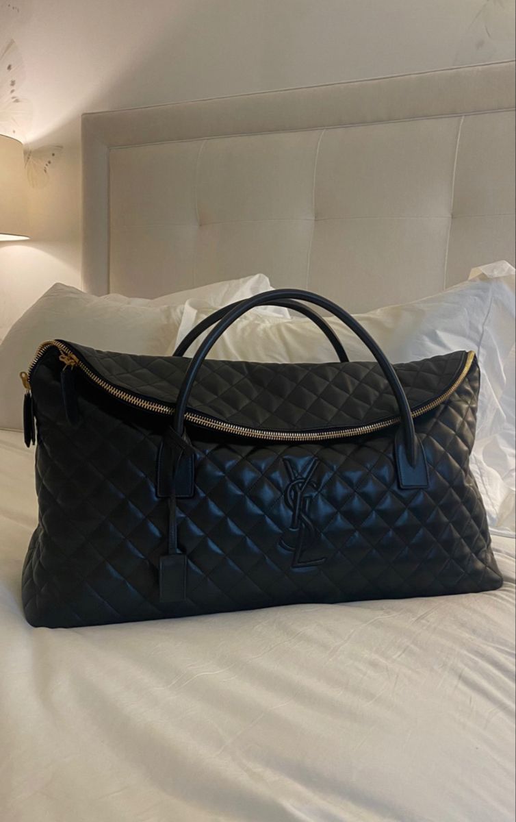 Black YSL Giant Quilted Leather Weekend Duffle Bag Black quilted handbag on a bed with a neutral headboard