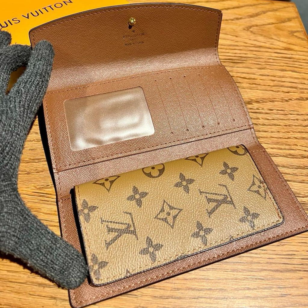 Brown Louis Vuitton Wallet leather wallet with monogrammed lining on a wooden surface, with a Louis Vuitton box in the background.