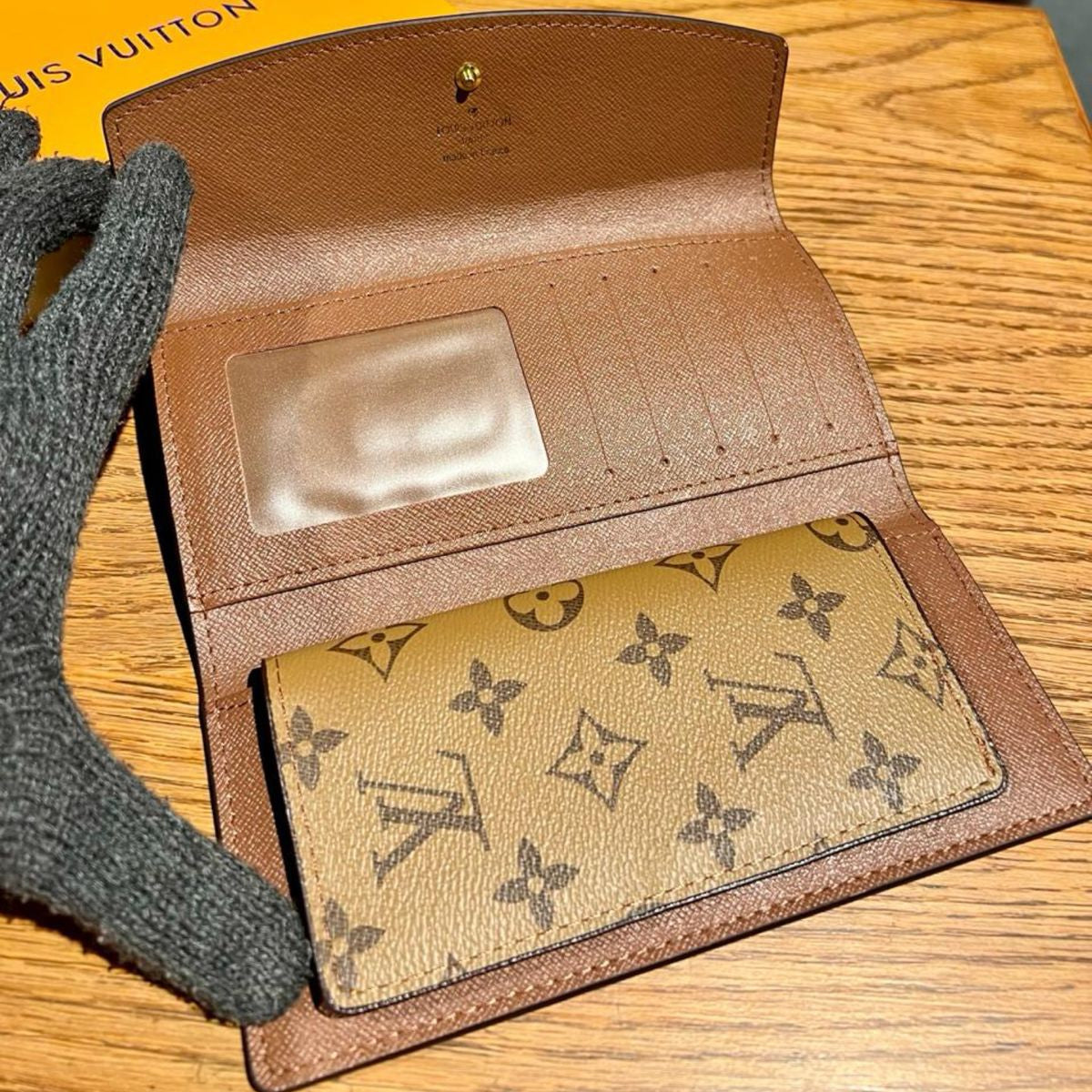 Brown Louis Vuitton Wallet leather wallet with monogrammed lining on a wooden surface, with a Louis Vuitton box in the background.