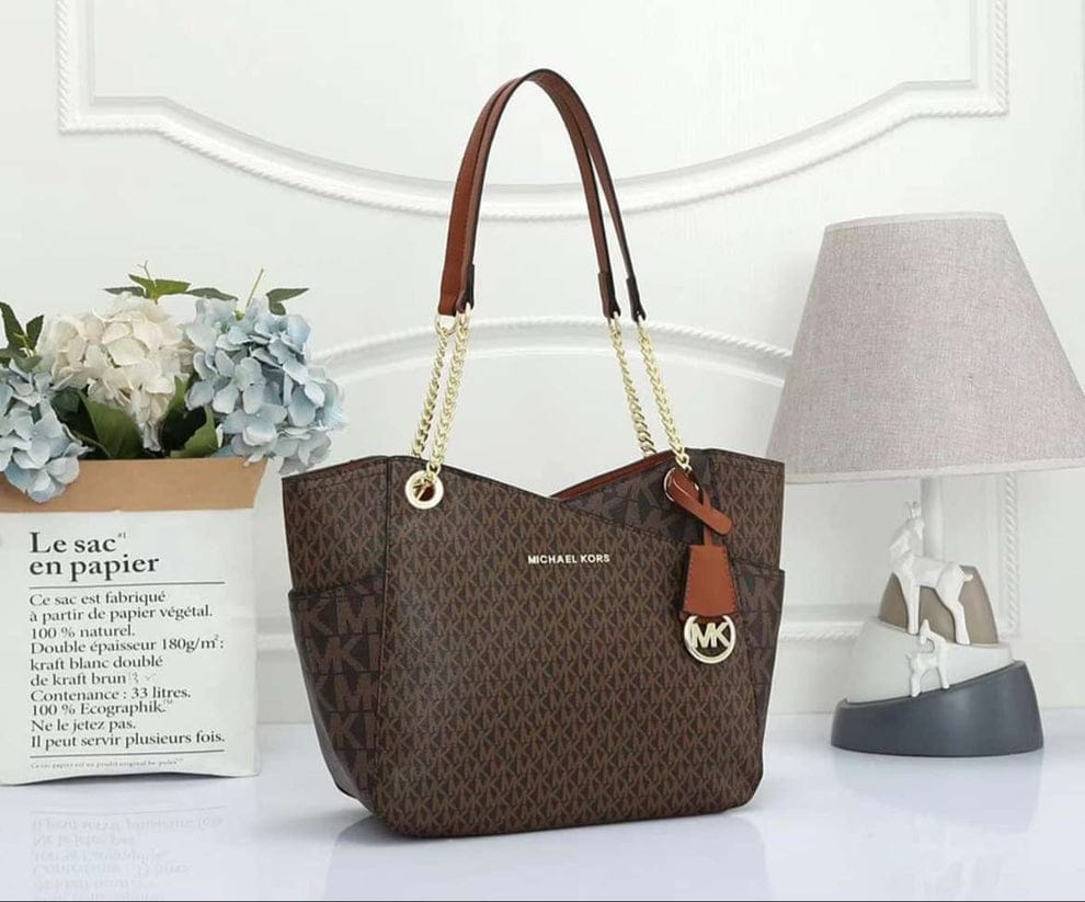 Tan Michael Kors Signature Tote Bag Brown handbag with gold chain and logo on a white surface with decorative items.