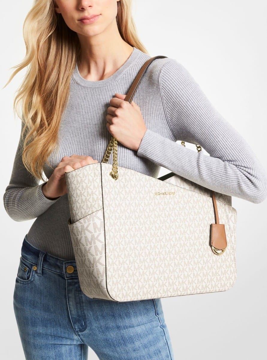 White Michael Kors Signature Tote Bag.Woman holding a beige quilted handbag with a gold chain detail on a light gray background