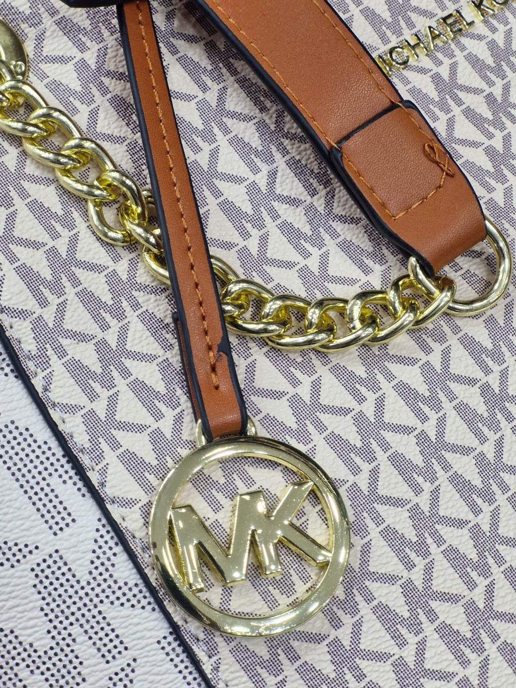 White Michael Kors Signature Tote Bag Close-up of a handbag strap with gold chain and logo on a patterned background