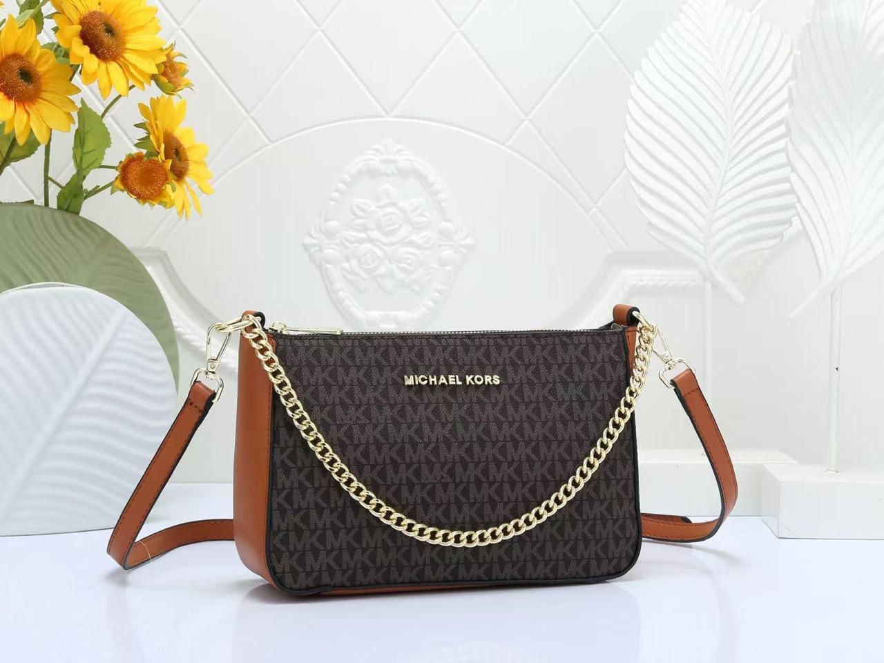 Tan Michael Kors Chain Sling Bag handbag with gold chain detail on a white surface with sunflowers in the background