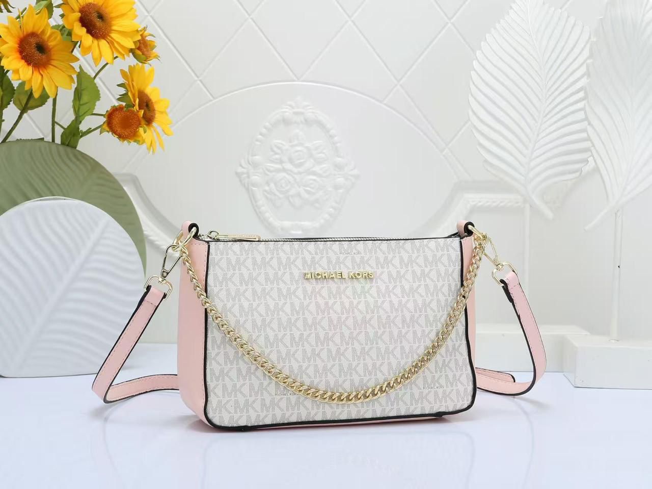 Pink Michael Kors Chain Sling Bag handbag with gold chain and pink accents on a white surface with sunflowers in the background