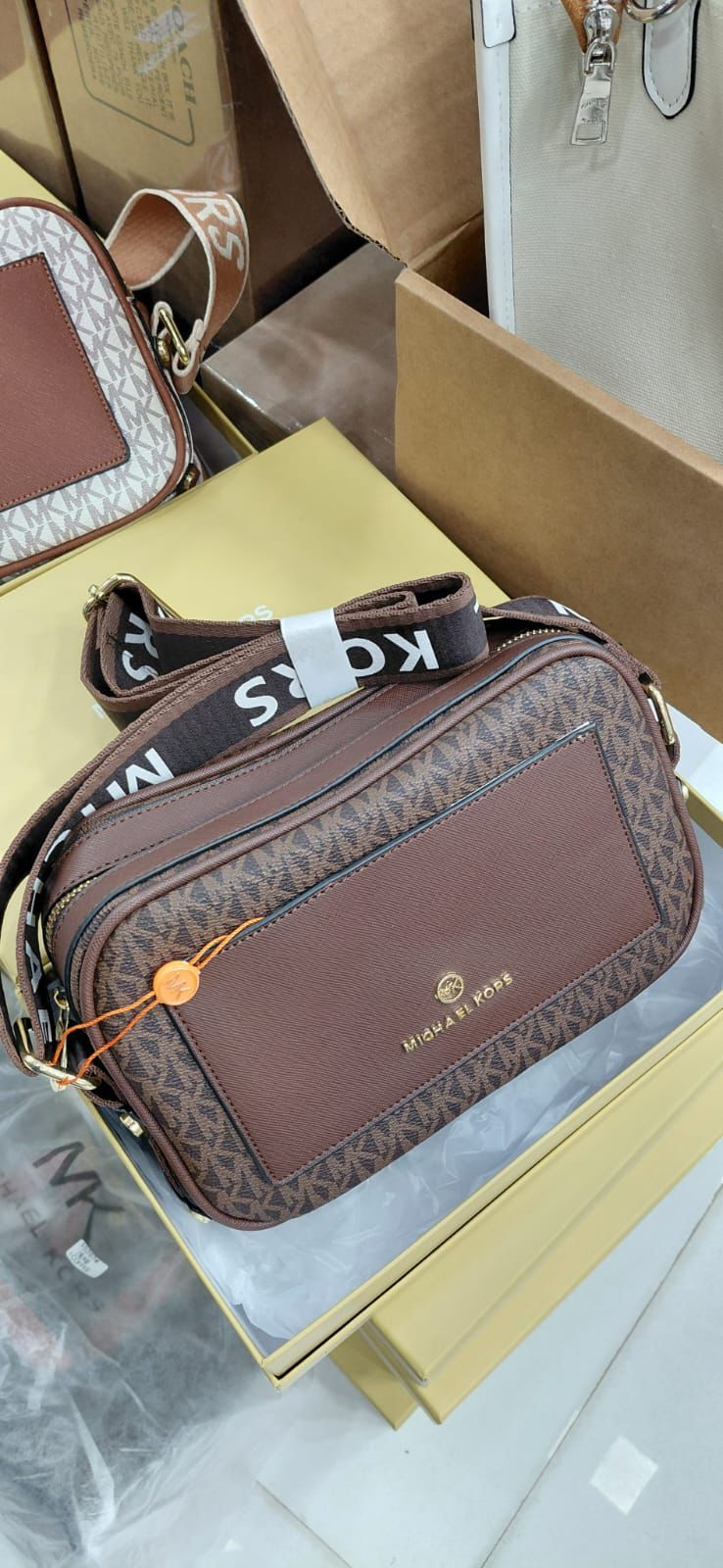 Tan Michael Kors Kinsley Sling Bag .Brown handbag with visible branding on a gold surface