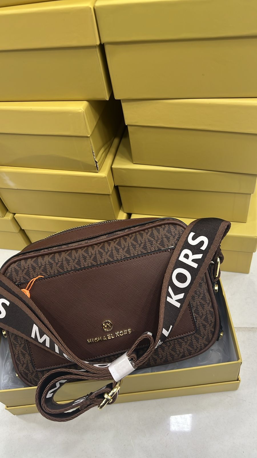 Tan Michael Kors Kinsley Sling Bag Brown handbag with 'Kors' branding on a white surface with yellow boxes in the background
