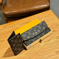 Black Louis Vuitton wallet on a wooden surface with a yellow box