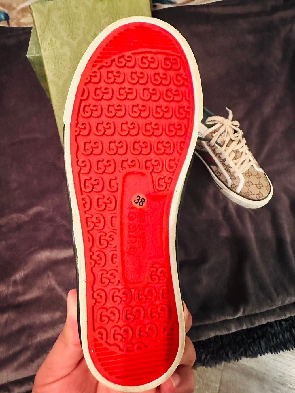 Gucci sneakers Close-up of a red sole with a pattern, held against a dark fabric background.