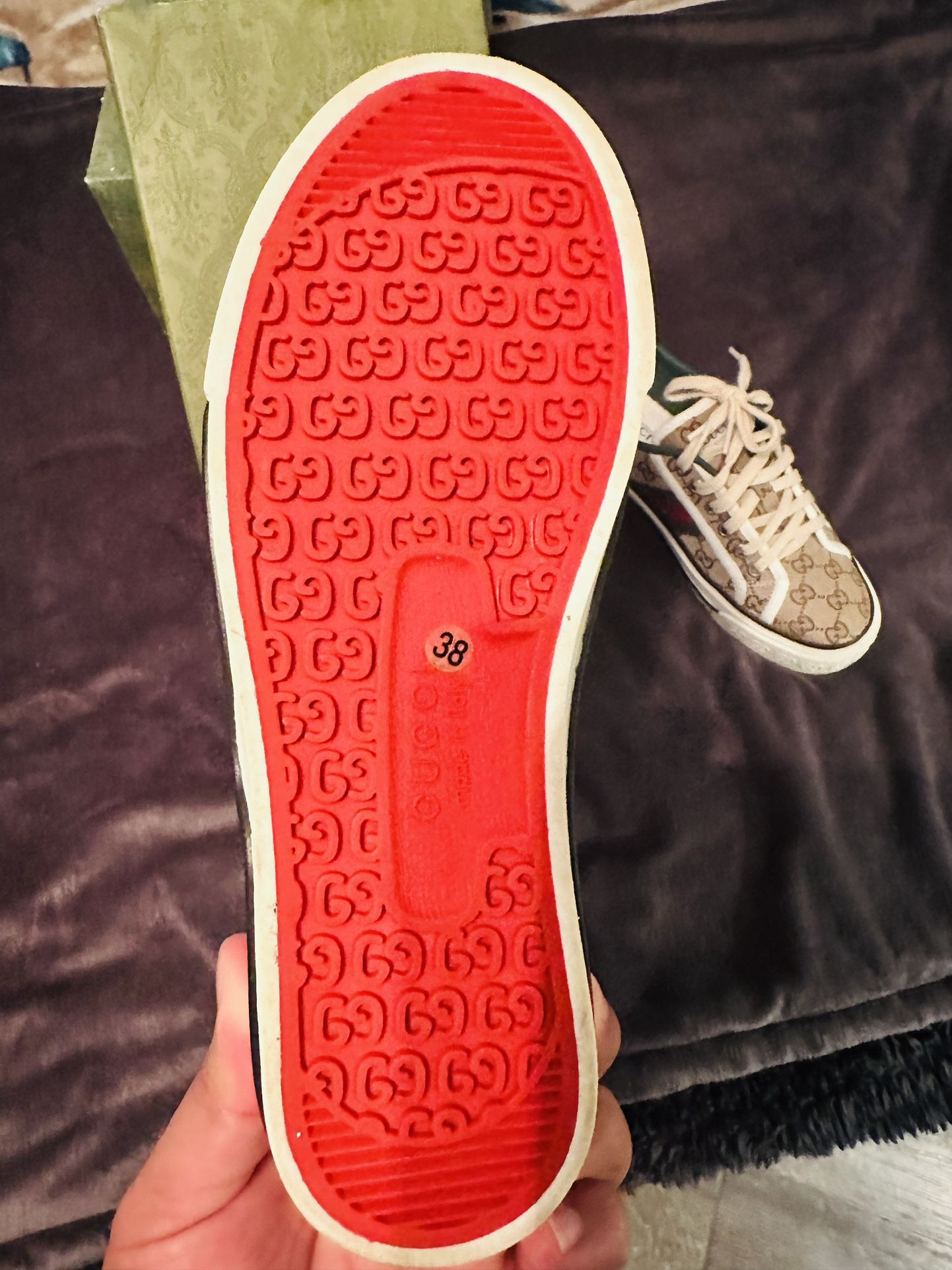 Gucci sneakers Close-up of a red sole with a pattern, held against a dark fabric background.