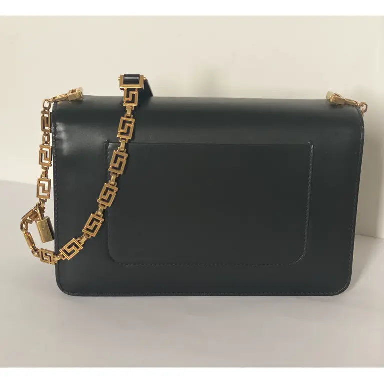Black medusa handbag with a gold chain strap on a light background