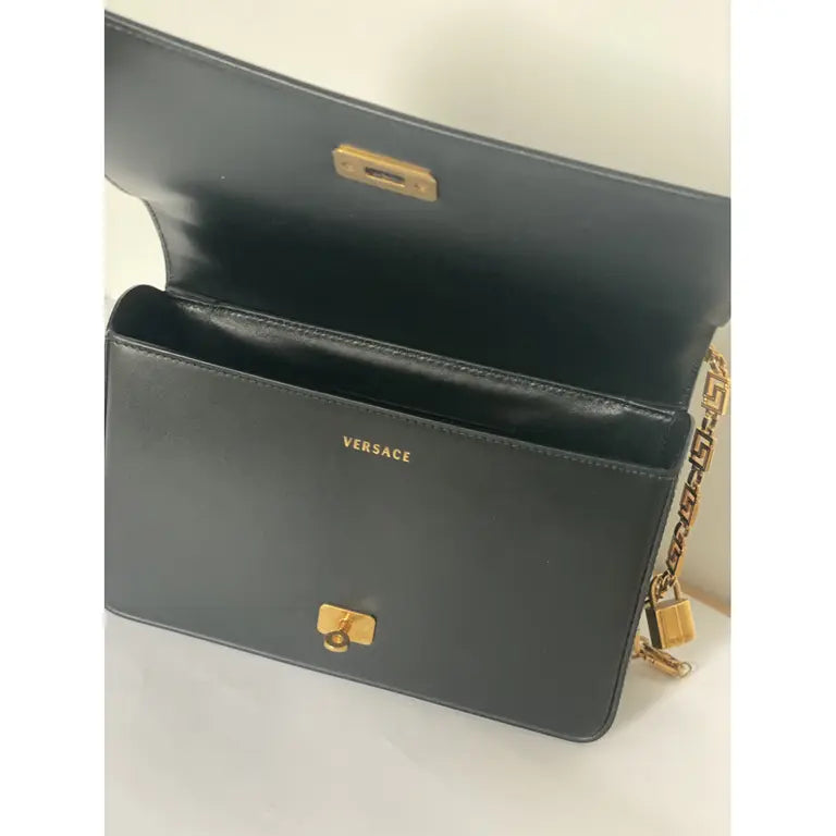 Black medusa Versace handbag with gold accents on a light background