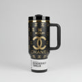Black tumbler with gold branding against a background of fashion brand names