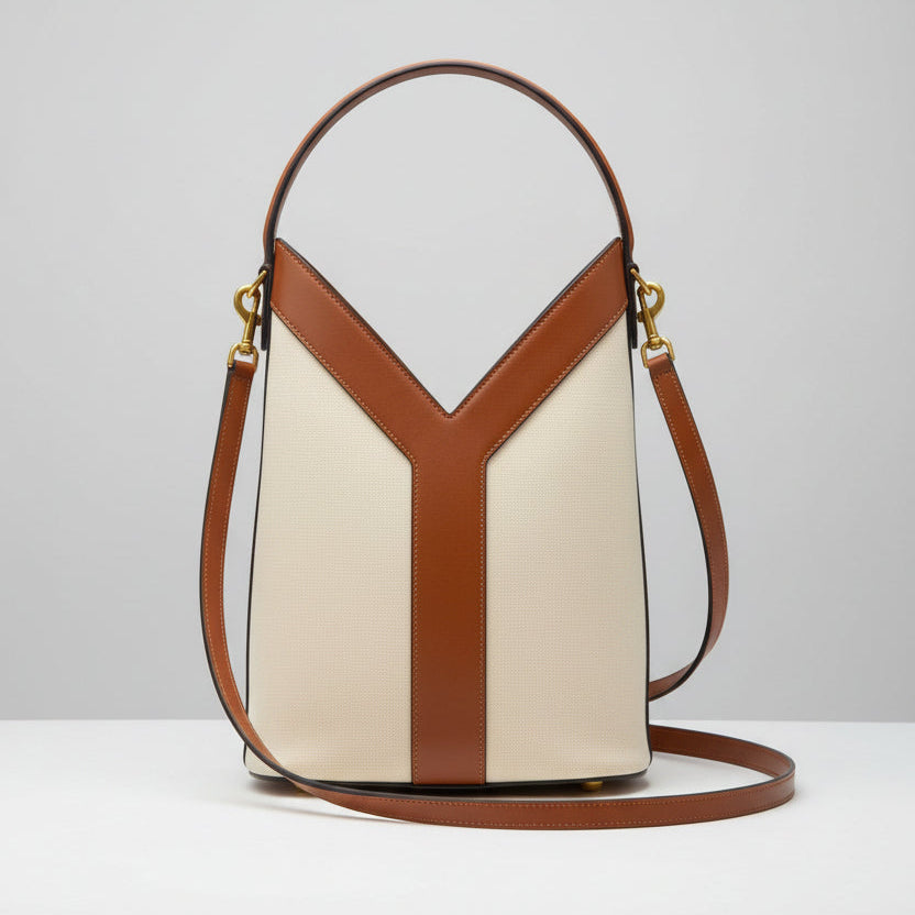 Beige YSL Y Top Handle Bucket Bag Handbag with a distinctive Y-shaped design on a white surface with a black and gold striped background.