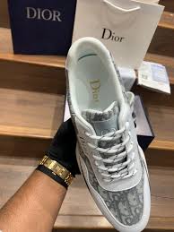 Person holding a Dior sneaker with a Dior box in the background